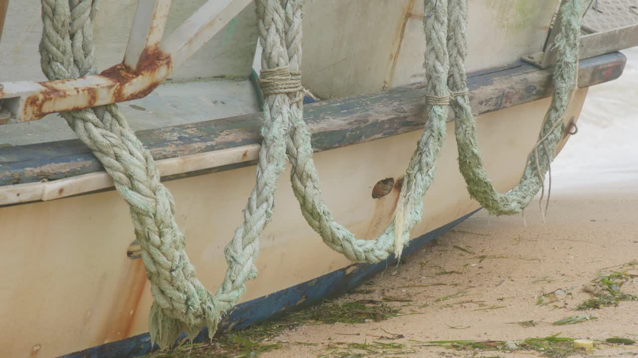 A commercial fishing vessel, pushed onto remote beach by recent heavy monsoon storms, now sits on side. Port side with ropes, clip 8