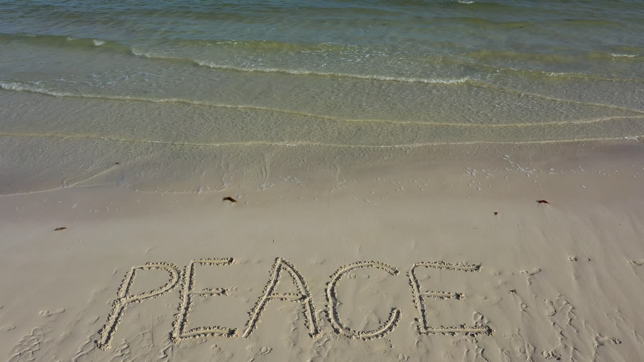 Turning shot of PEACE inscribed in the sand on a beach