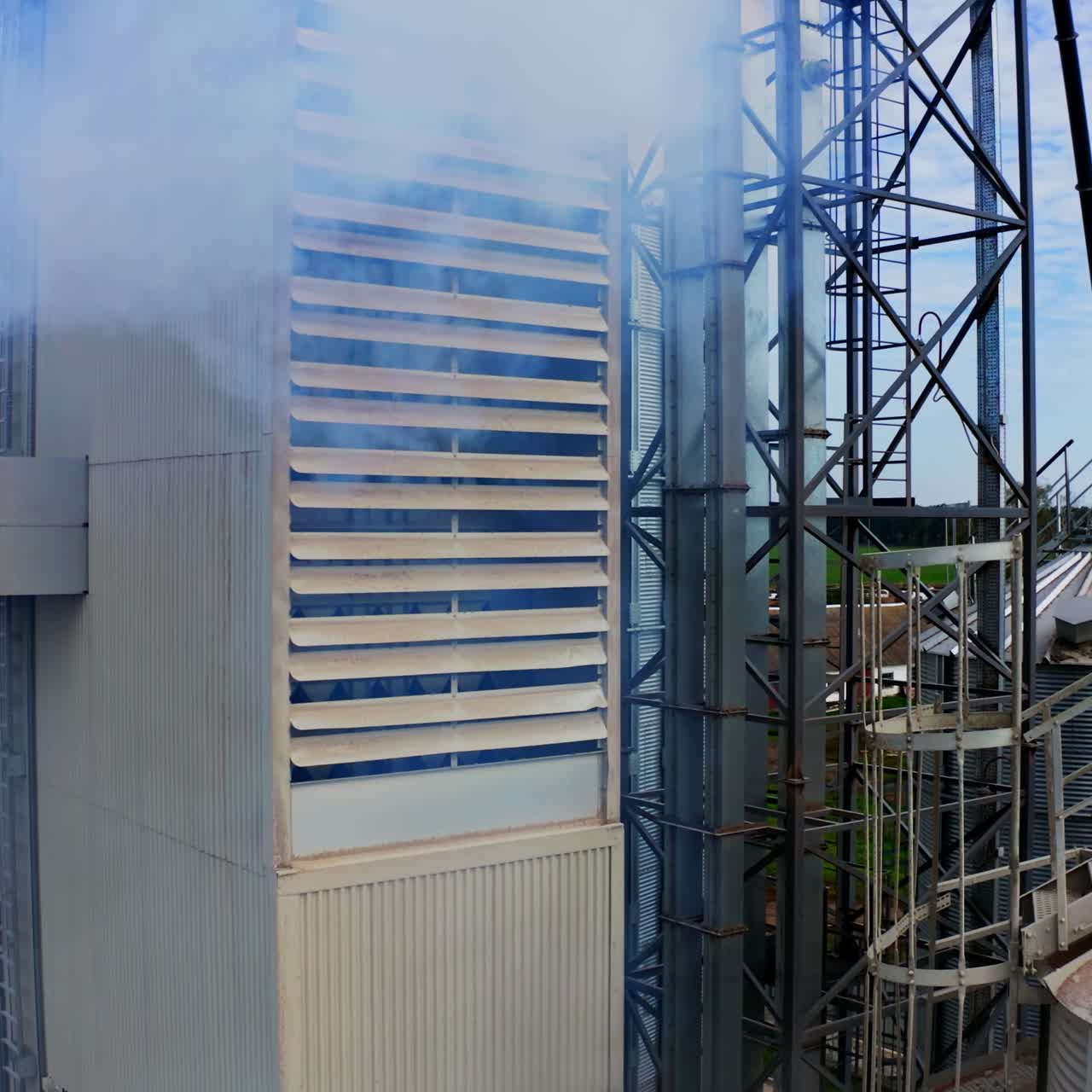 Exterior of modern industrial plant. White smoke filling in the air from warehouse. Close-up. Pollution the environment. Camera rising up.