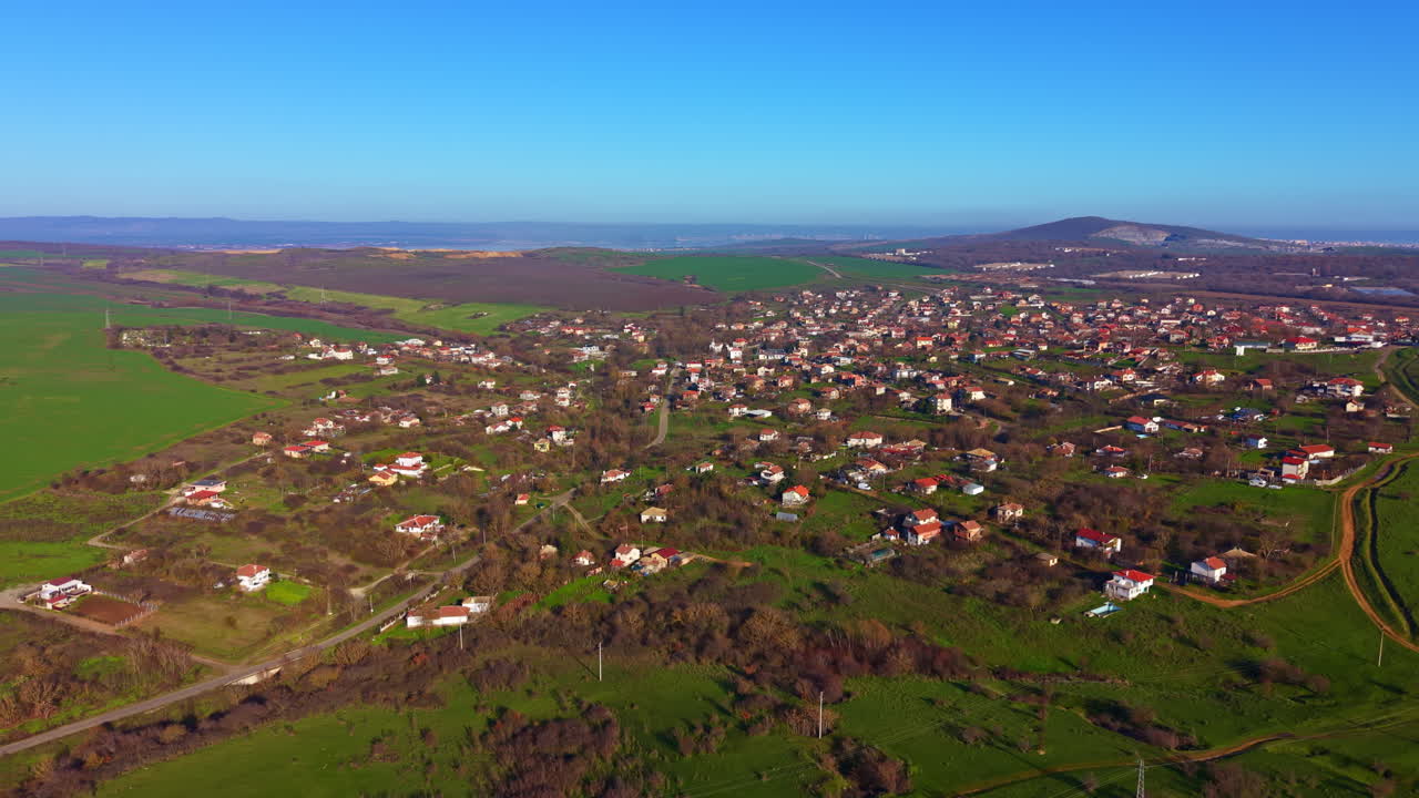 Store grønne åser omfavner en fredelig landsby under en strålende blå himmel på en solrik morgen