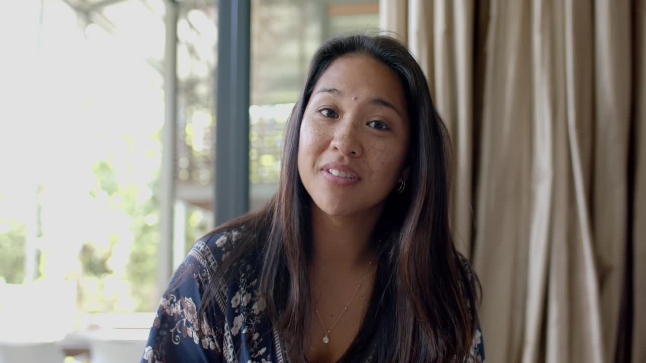 행복한 아시아 여성이 비디오 통화를 하고 이 나는 거실에서 미소 짓고, 느린 동작