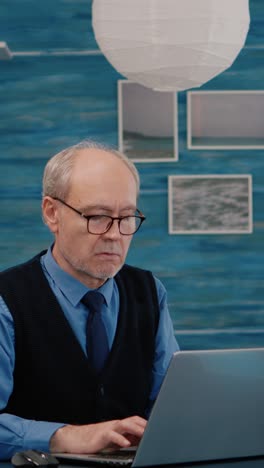 vertical video: elderly man freelancer opening laptop squinting while reading emails