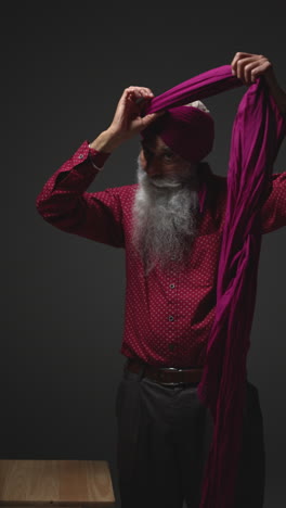 a man wearing a pink turban, standing with a wooden table folded beside him.