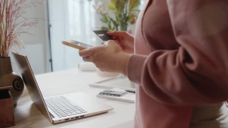 mujer de cultivo haciendo compras en línea en su teléfono inteligente. mujer irreconocible con ropa rosa ingresando las credenciales de la tarjeta de crédito en el teléfono inteligente mientras paga por un pedido en línea