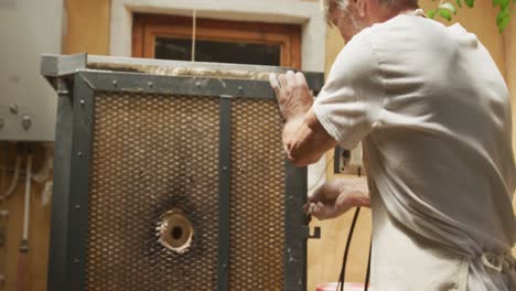 Senior-caucasian-man-wearing-apron-firing-pots-in-kiln-at-pottery-workshop