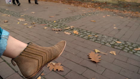 woman's foot in brown ankle boots while sitting with people passing by at oliwski park in gdansk, poland