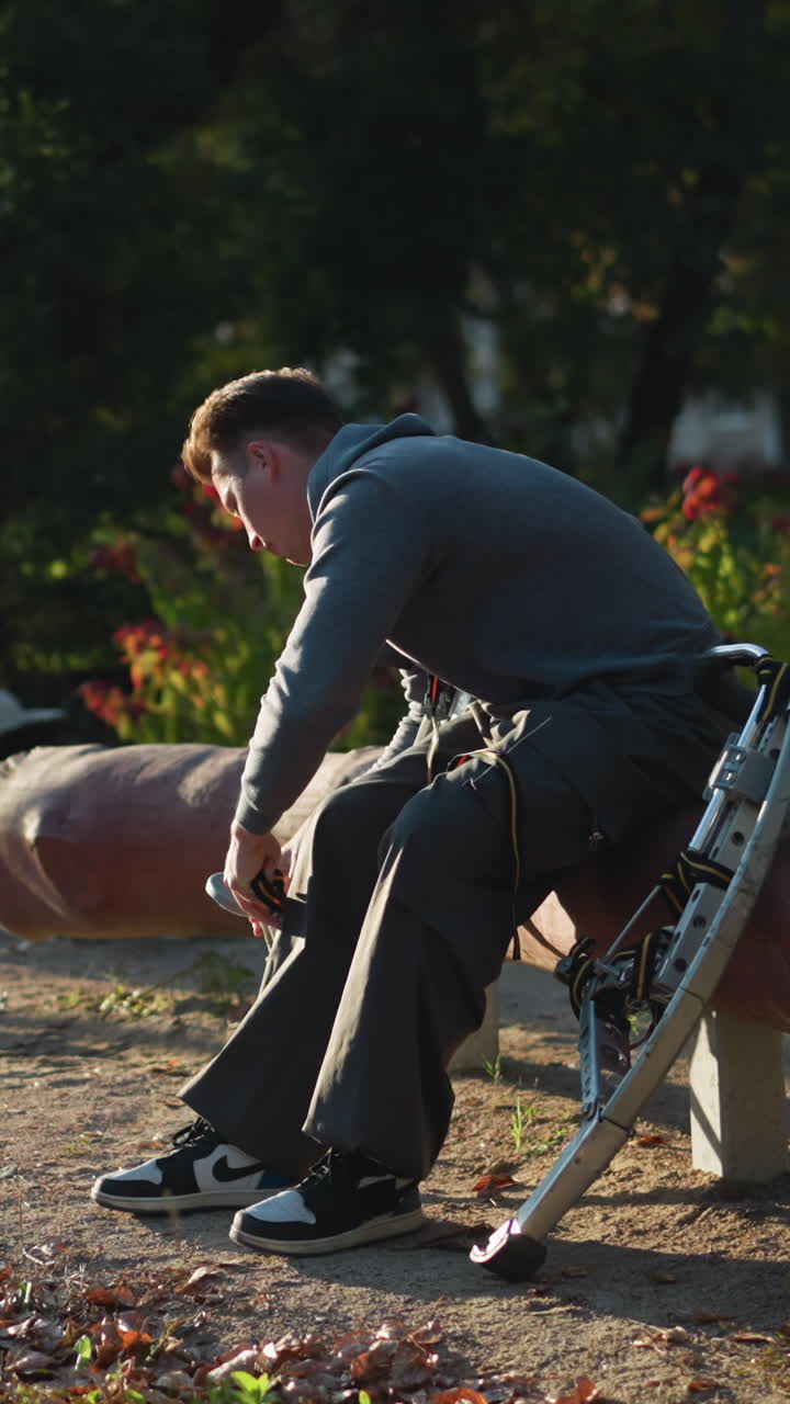 chap sentado en madera al aire libre en sudadera de capucha gris oscuro y pantalones de sudadera, intensamente enfocado en el ajuste de pilotes cargados de resorte. rodeado de árboles y vegetación en un entorno natural pacífico