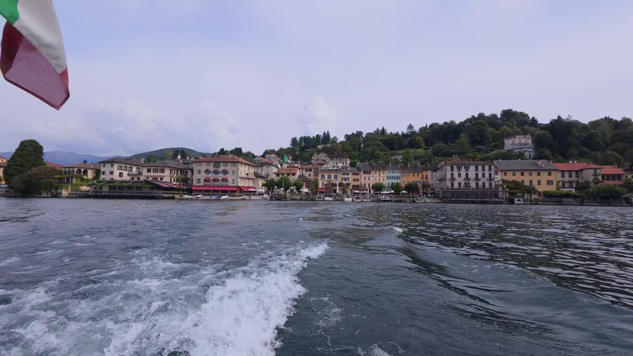 A scenic view from a boat on the lake, leaving San Giulio Island with charming Italian architecture under a clear sky.