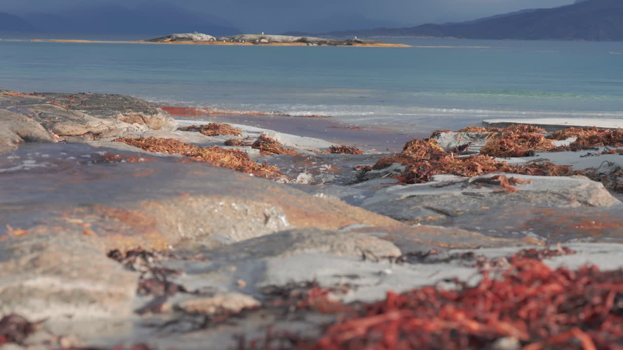A shallow stream flows over the rocks the sandy beach