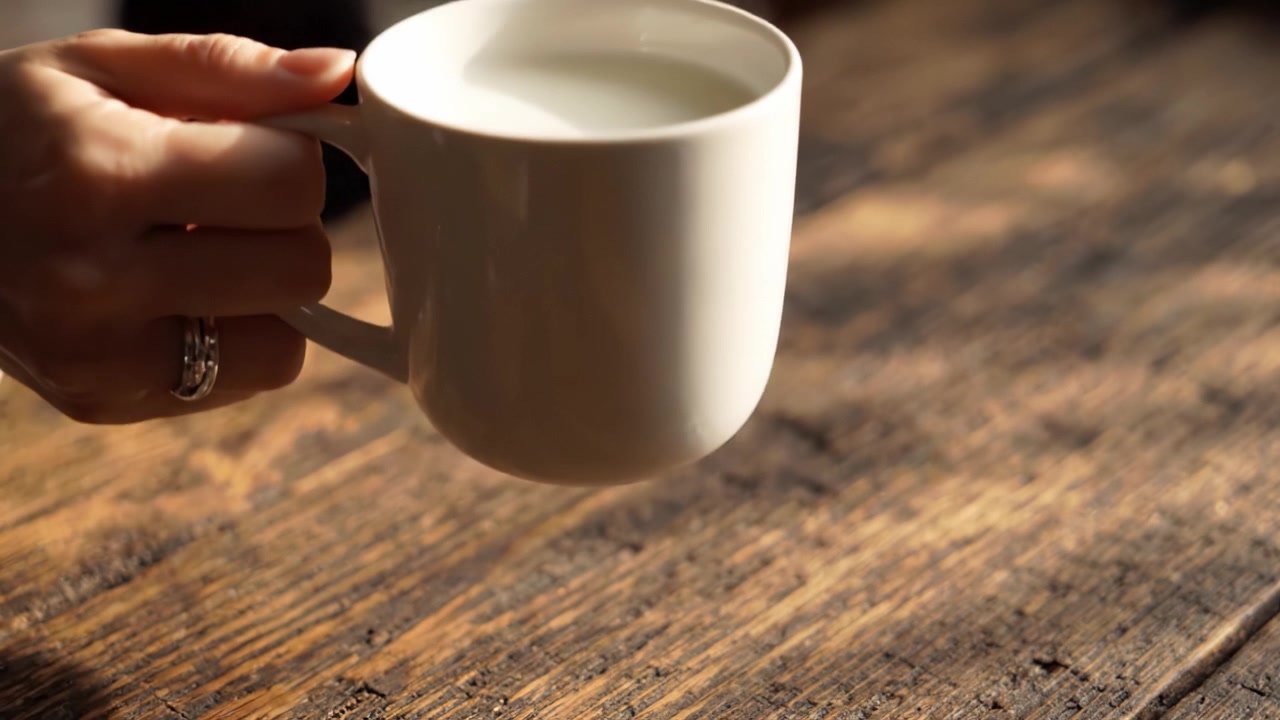 Un momento sereno: primo piano di una tazza di ceramica bianca piena di latte su un tavolo di legno rustico, che evidenzia l'atmosfera calma dell'ambiente circostante.