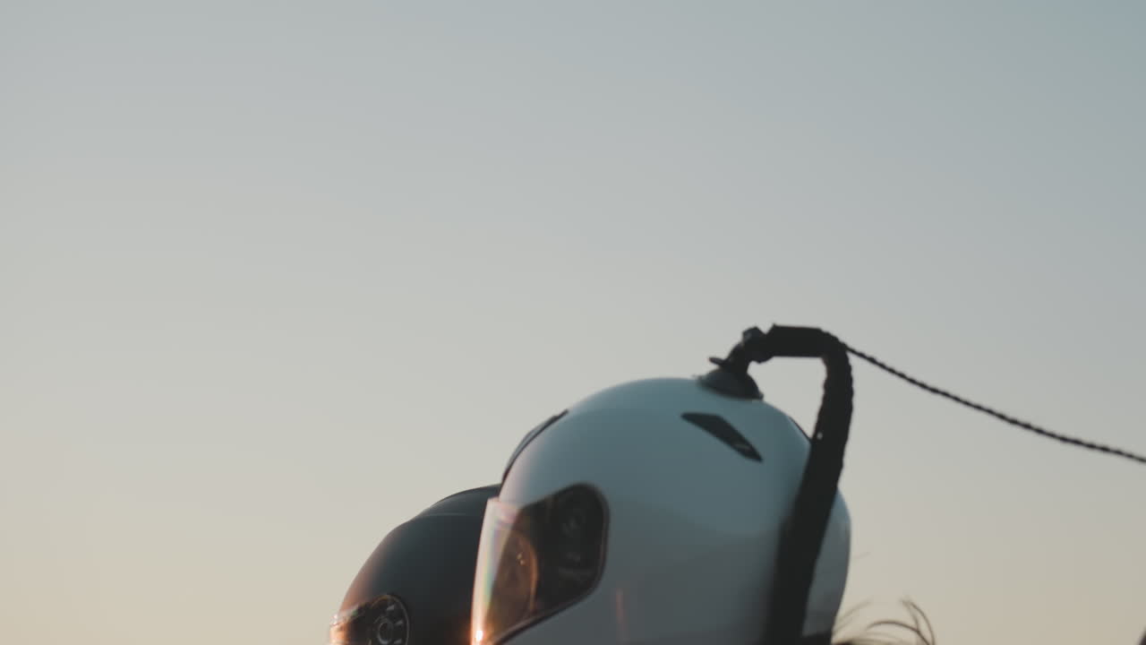 Passenger wearing helmet rides on motorcycle as long hair sways in wind against warm sunset sky, capturing freedom, lifestyle, and emotion of open road travel with vibrant evening atmosphere