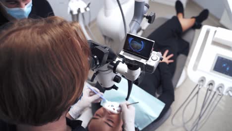 professional dentist treats teeth of a young woman. stomatologist examines patient's teeth through the modern microscope. new technologies in medicine.