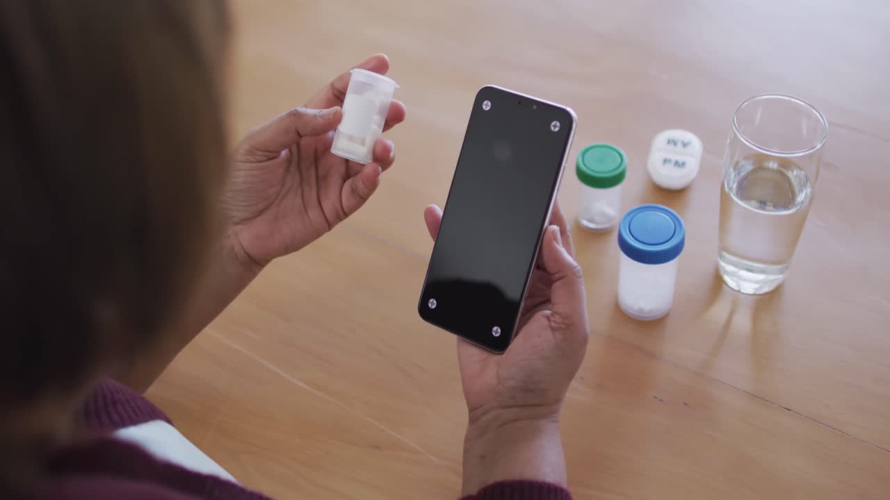 mujer mayor afroamericana haciendo usando teléfono inteligente y sosteniendo medicamentos, copia espacio en la pantalla
