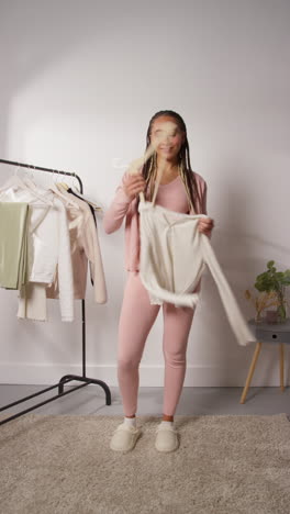 video vertical de una influencer femenina de redes sociales produciendo contenido generado por el usuario en el estudio probando una variedad de trajes de moda filmados en tiempo real 1