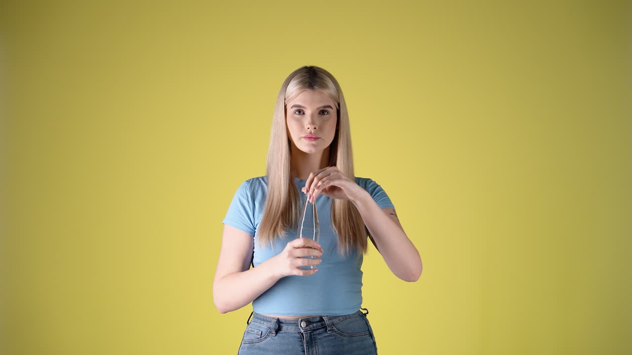 una joven rubia caucásica bebe una botella de agua de vidrio en un estudio de fotografía corporal.