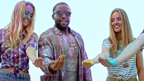 beautiful cute two blond girls and stylish guy in dark glasses tossing colorful paints in powder up in the air and having fun at the holi celebration