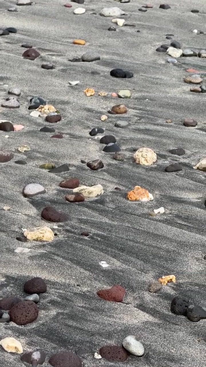 Onde che si infrangono su sabbia vulcanica scura e ciottoli sulla spiaggia
