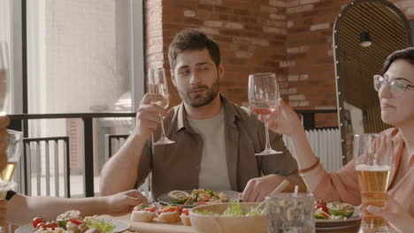 caucasian young man makes a toast with his group of friends at a dinner party. multiracial friends reunion.