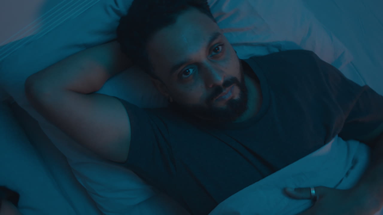 Sleepless Man Lying in Bed with Wife and Looking at Camera