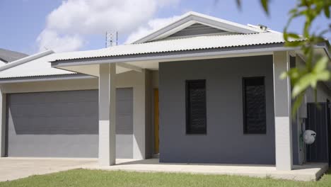 front of a newly built ground-level grey house with green lawns and a roller door garage