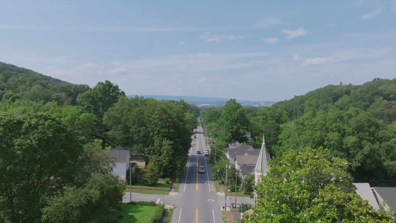 Drone footage looking down a straight, tree-lined road in St. Elmo, Chattanooga, framed by forested hills and historic homes on either side