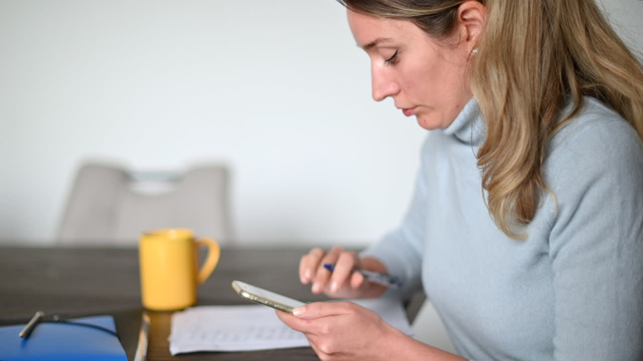Woman working on mobile phone and writing at the office