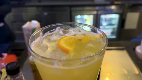 a bartender in formal attire prepares a citrus cocktail at a modern bar in bangkok, under cool ambient lighting, with steady camera focus on the drink