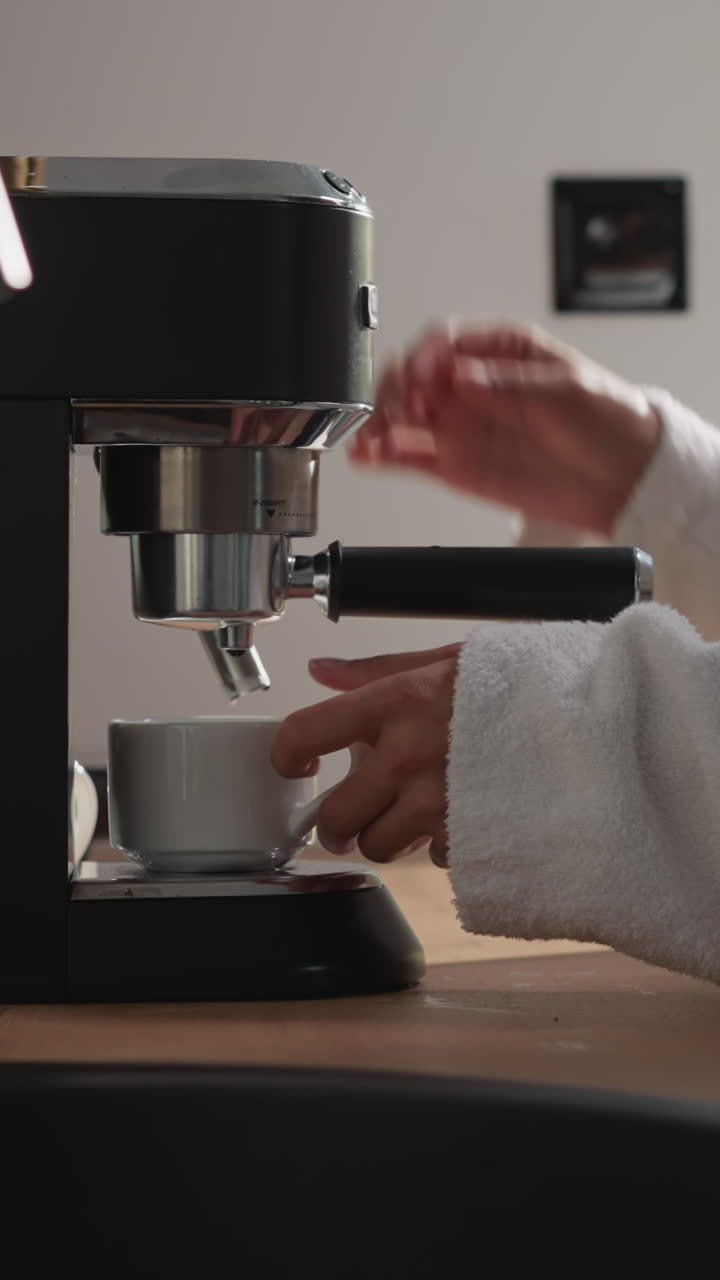 여성은 부에서 커피 머신에 컵을 니다. 쾌적한 옷을 입은 여자는 집에서 커피 메이커에서 뜨거운 강한 음료로 컵을 채니다.