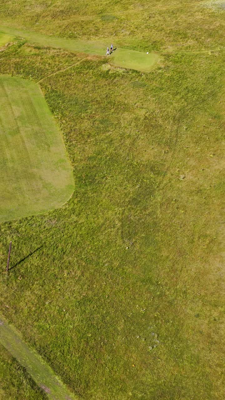 Drone captures golfers walking on green fairway, bright daylight, wide landscape, smooth aerial movement