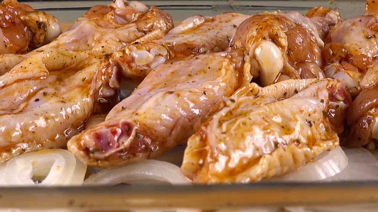 Le ali di pollo marinate sono disposte sugli anelli di cipolla in una pirofila di vetro