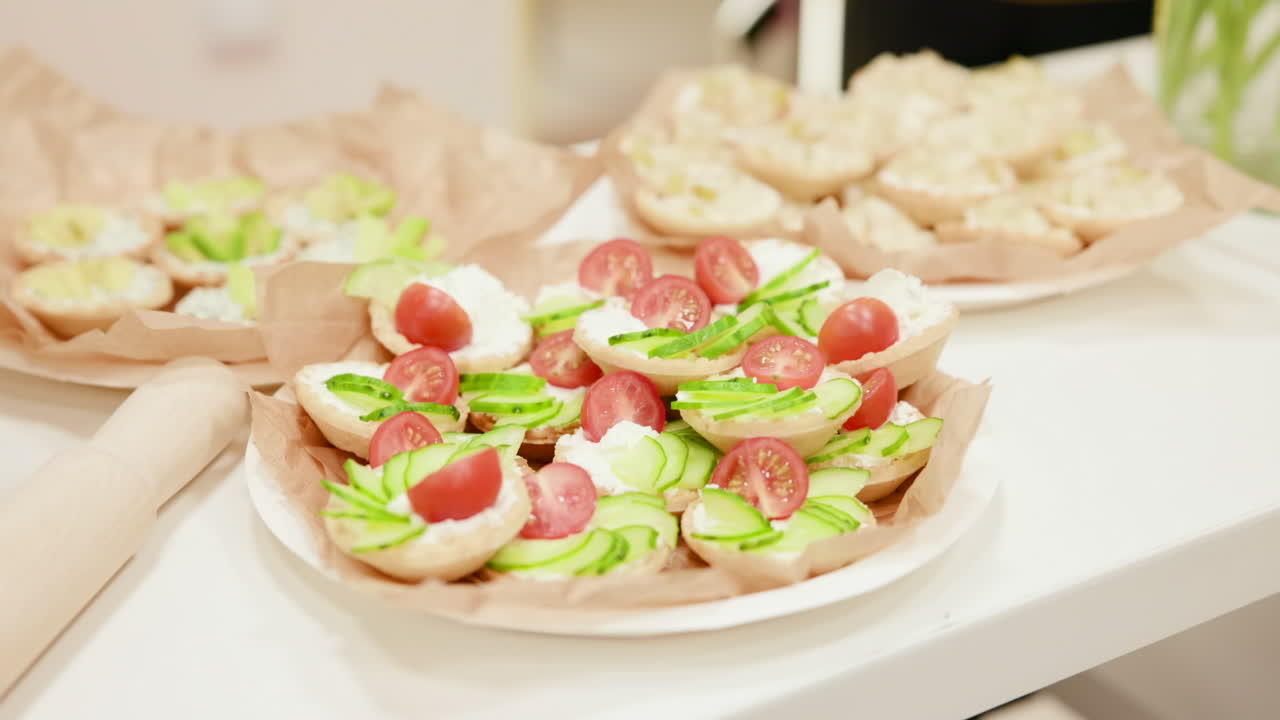 Piatto di canapè freschi con avocado, pomodori, formaggio cremoso e basilico in cestini di pasta sfoglia croccante su un vassoio foderato di carta