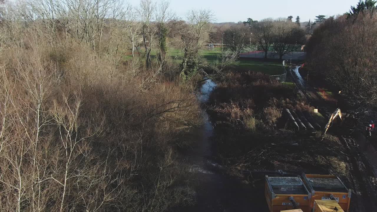 Aerial along the River Lambourn and through woods with engineering works including excavators