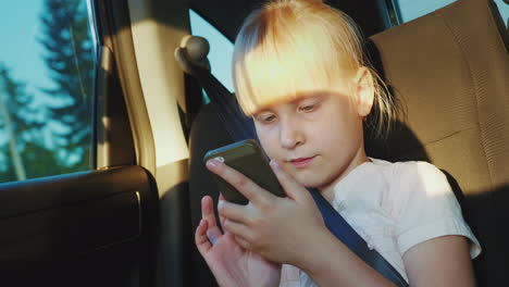 Das-Mädchen-Reist-In-Einem-Auto-Und-Spielt-Auf-Einem-Smartphone-Auf-Der-Straße-Mit-Einem-4k-Video-Für-Kinder