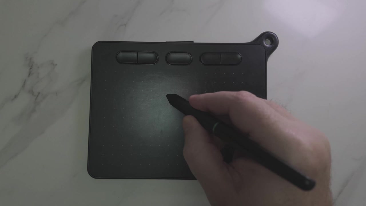 Artist hand uses a black stylus to sketch fluid wave and heart designs across digital graphics pad resting on a marble desk