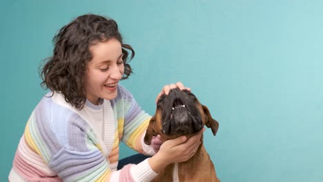young woman feeding obedient dog on blue background