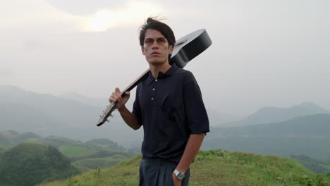 Modern-asian-handsome-guy-walking-with-a-winning-attitude-with-his-guitar-on-shoulder-at-sunset