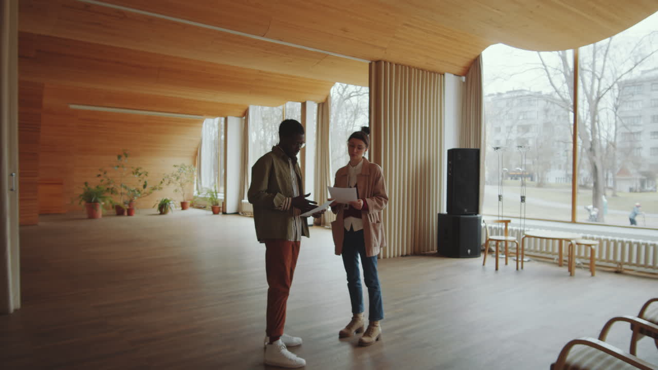 Diverse Man and Woman Discussing Documents in Modern Auditorium