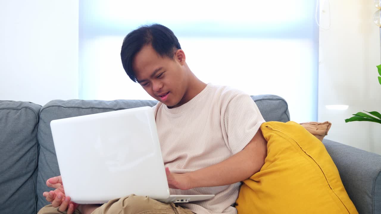 Serious Young asian man with Down syndrome using laptop while sitting on sofa