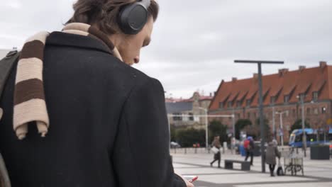 stylish guy in scarf and coat listen a music on streaming service by using mobile phone