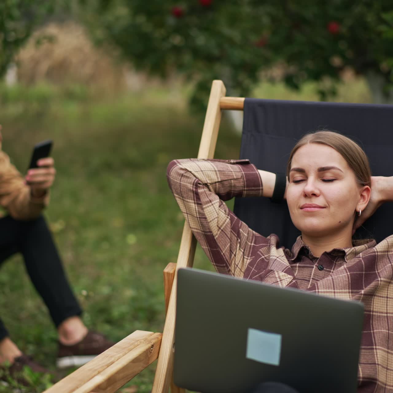 Para młodych osób pracujących zdalnie siedzi w sadzie jabłoniowym. Nowocześni freelancerzy z pozytywnym nastawieniem korzystają z urządzeń, pracując na łonie natury w relaksującej atmosferze.