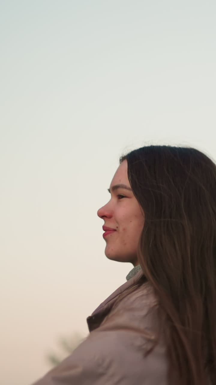 una vista de cerca de una mujer joven con una chaqueta de melocotón, disfrutando de un momento de patinaje con una expresión alegre en su rostro. el fondo presenta un cielo suave y pastel al atardecer