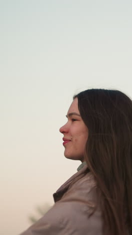 una vista de cerca de una mujer joven con una chaqueta de melocotón, disfrutando de un momento de patinaje con una expresión alegre en su rostro. el fondo presenta un cielo suave y pastel al atardecer