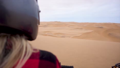 slomo over the shoulder of young blond woman with helmet on quad bike overlooking namibian desert