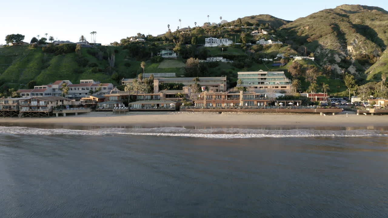 Aerial View of a Serene Coastal Beach with Waterfront Buildings and Green Hills