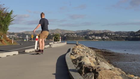 mężczyzna jadący na deskorolce longboard z dala od kamery obok oceanu