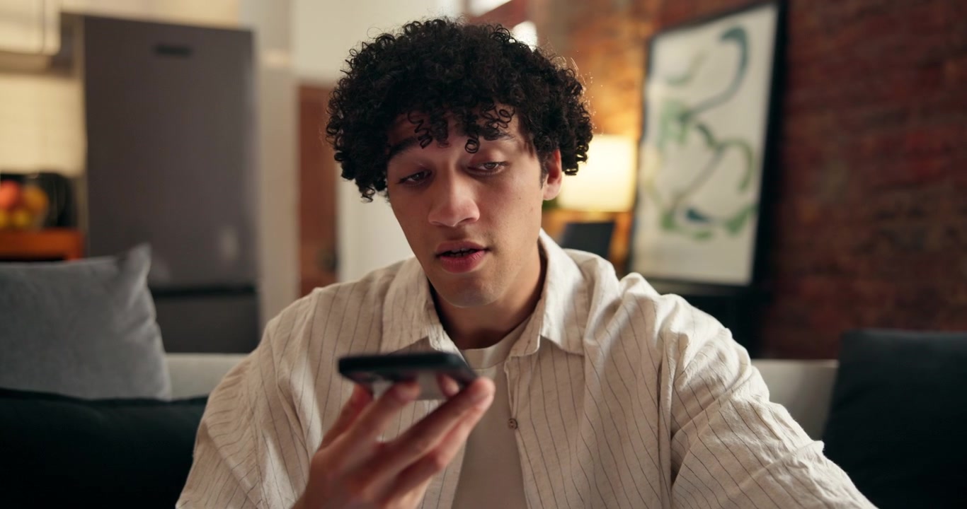 Young Man Recording Voice Message on Smartphone at Home