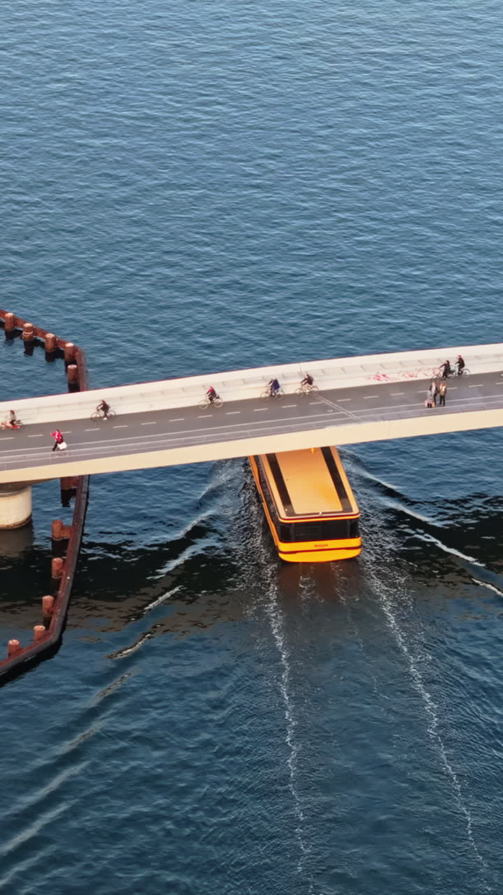Aerial drone view of a yellow boat moving on the water under the Quay Bridge across the port of Copenhagen, Denmark in the evening. Vertical