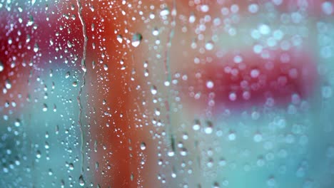 glass window in a rainy day with drops. transparent water of raindrops on a glass surface with red background. close-up.