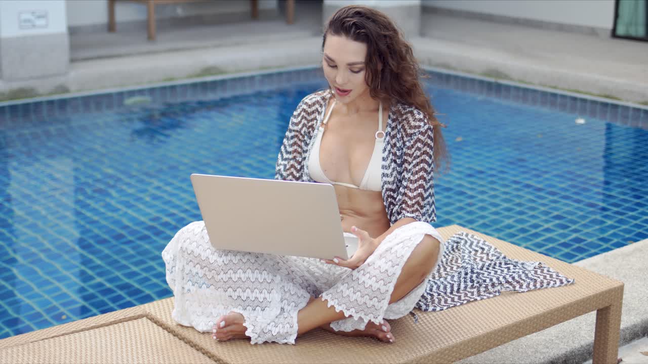 mujer usando laptop junto a la piscina