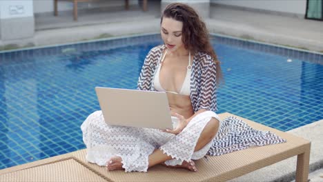 Woman-using-laptop-on-poolside